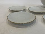 four white and gold plates and a bowl on a white table