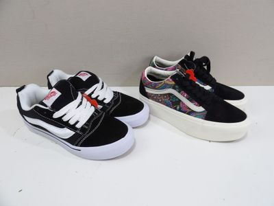 deux paires de baskets de style « Vans » noires et blanches posées sur une surface blanche