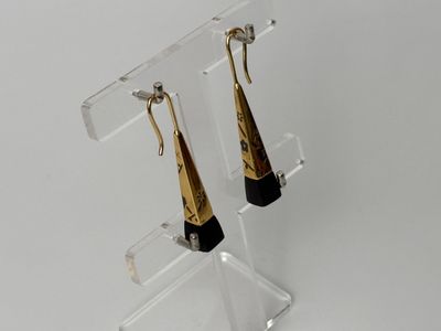 pair of gold and black earrings on a clear acrylic stand