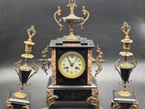 a black and gold clock sitting on top of a table next to three vases