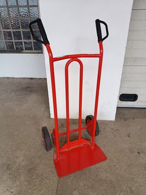 un diable rouge avec une poignée noire sur le trottoir