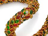 a close up of a gold bracelet with green, red and white stones