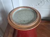 a red vase sitting on a table with a clock on top of it
