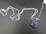 une chaîne en argent avec un pendentif orné d'une pierre bleue, posée sur une surface noire