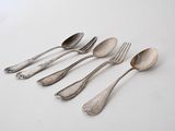 six spoons and a fork are lined up on a white surface