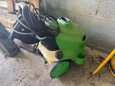 un aspirateur vert et noir et un tuyau jaune posé par terre