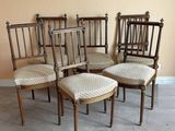 six chaises anciennes aux assises rembourrées sont alignées contre un mur beige