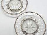 two clear glass plates with silver rims on a white surface