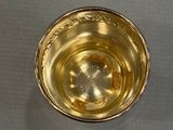 a gold cup sitting on a table next to a silver plate