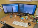 two computer monitors sitting on a desk with a keyboard and mouse