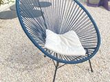 une chaise bleue posée sur un sol en gravier, à côté d'une table et de chaises