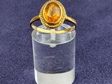 gold plated ring with a citrine stone in the center on a clear glass