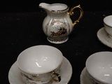 four cups and saucers on a table with a pitcher