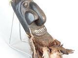 a wooden mask on a stand with feathers on it