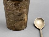 a silver cup with a spoon next to it on a table
