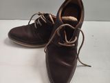 une paire de chaussures en cuir marron à lacets posée sur une surface blanche