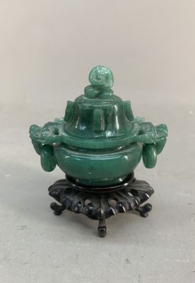 brûleur d'encens en forme de Bouddha en jade vert, posé sur un socle, sur une surface blanche