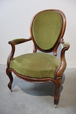une vieille chaise dont l'assise est recouverte de tissu vert, dans une pièce