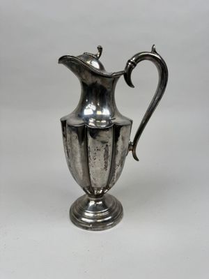 un pichet ancien plaqué argent posé sur un socle, sur fond blanc