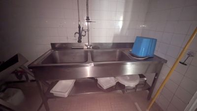 un lavabo en acier inoxydable dans une salle de bains avec une poubelle bleue