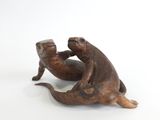 une paire de loutres en bronze, assises sur le dos sur une surface blanche