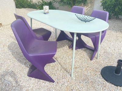 une table blanche avec des chaises violettes et un bol de fruits posé dessus