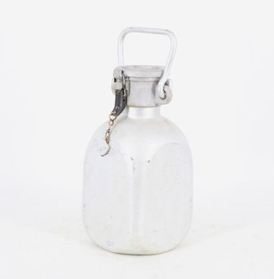 une bouteille en verre blanc munie d'une poignée en métal, posée sur une surface blanche