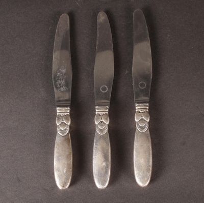 three silverplated knives and a knife holder on a black surface