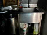 a sink in the corner of a kitchen with a trash can