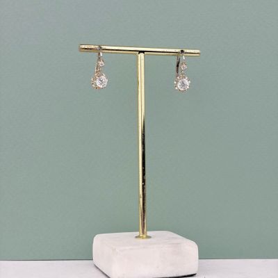 des boucles d'oreilles plaquées or posées sur un socle en marbre devant un mur vert