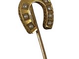 a gold horseshoe shaped brooch with pearls on it