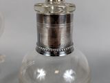 a small glass bottle with a silver lid next to a smaller glass bottle with a silver lid