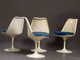 three white tulip chairs with blue cushions on a gray surface