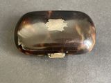 an antique tortoise shell cigarette case with a gold emblem on it
