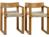 two wooden chairs with beige cushions on them against a white background