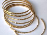 des bracelets rigides plaqués or empilés les uns sur les autres sur une surface blanche