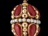 un gros plan sur une broche dorée et rouge ornée de perles