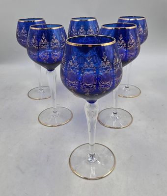 six verres à vin bleus bordés d'or, posés sur un fond blanc