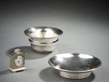 two silver dishes and a clock sitting on a table