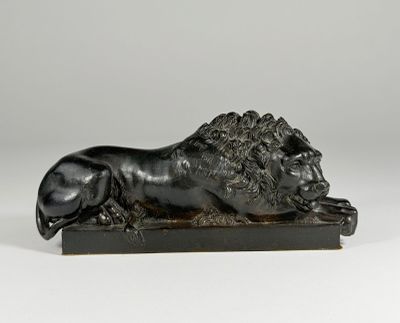 a black sculpture of a lion laying down on a wooden base