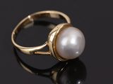 a gold ring with a white pearl on a black surface