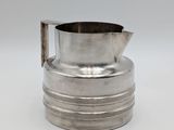 an old silver pitcher with a metal handle on a white surface