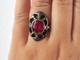 a close up of a person ' s hand holding a ring with a red stone
