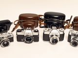 five old cameras lined up in a row on a white surface