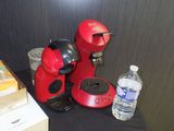 une cafetière rouge posée sur une table à côté d'une bouteille d'eau