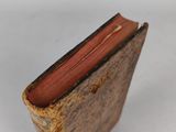 an old book with a red cover sitting on top of a white surface