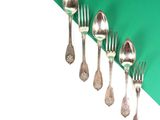 five silver spoons and two silver forks on a green and white background