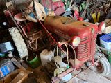 un vieux tracteur rouge dans un garage où se trouvent de nombreux autres objets