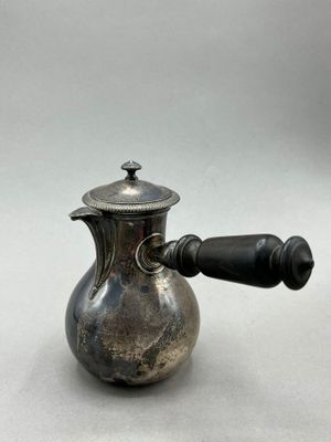 an antique silver coffee pot with a wooden handle on a white surface
