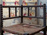 a wooden chair with a woven seat in front of a wallpapered wall